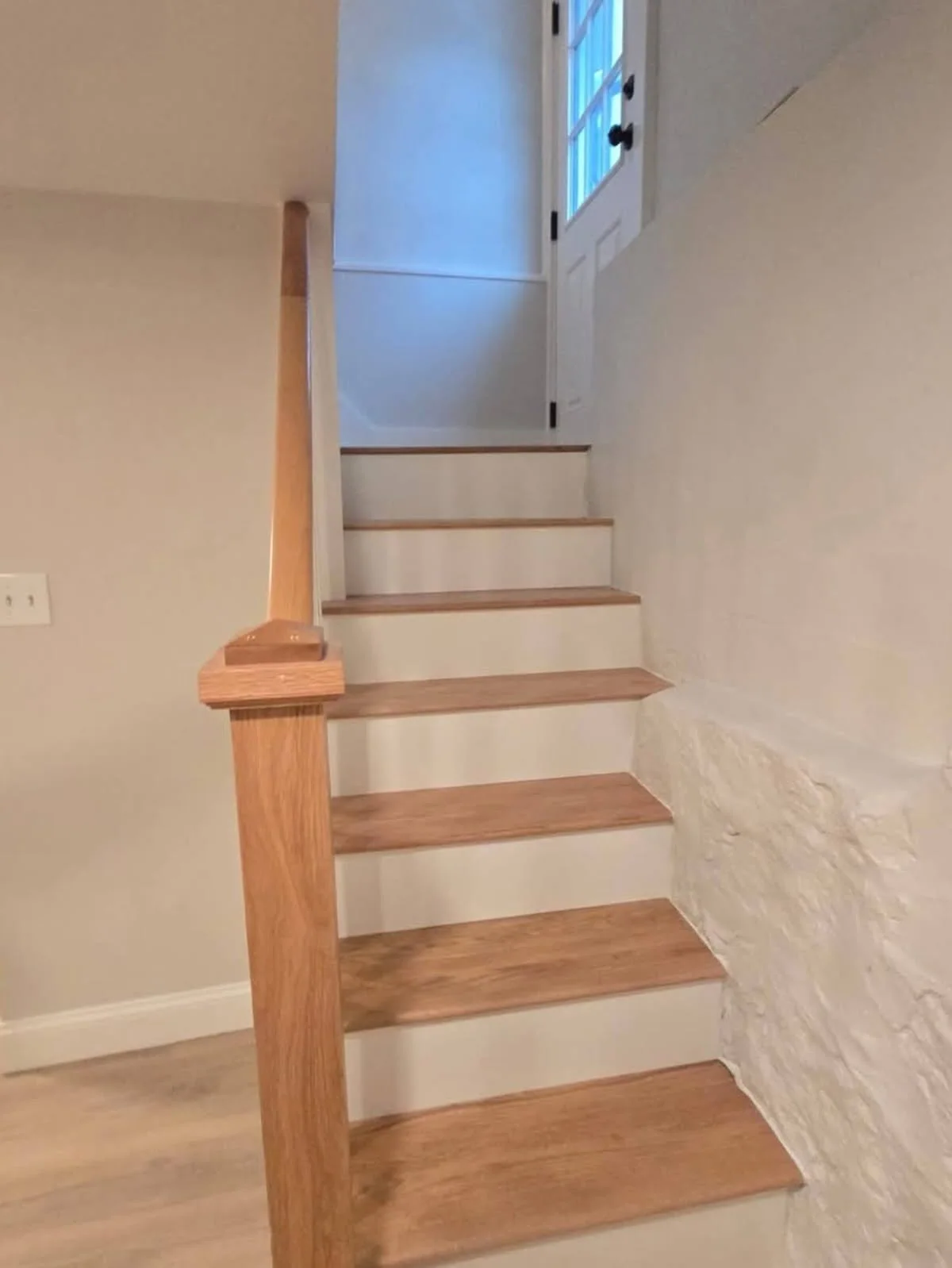 Rebuilt wooden staircase with warm natural-wood treads, crisp white risers, and a matching handrail