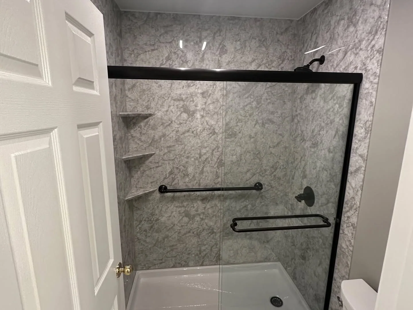 Renovated bathtub with gray stone-look tile, dark fixtures, and grab bars