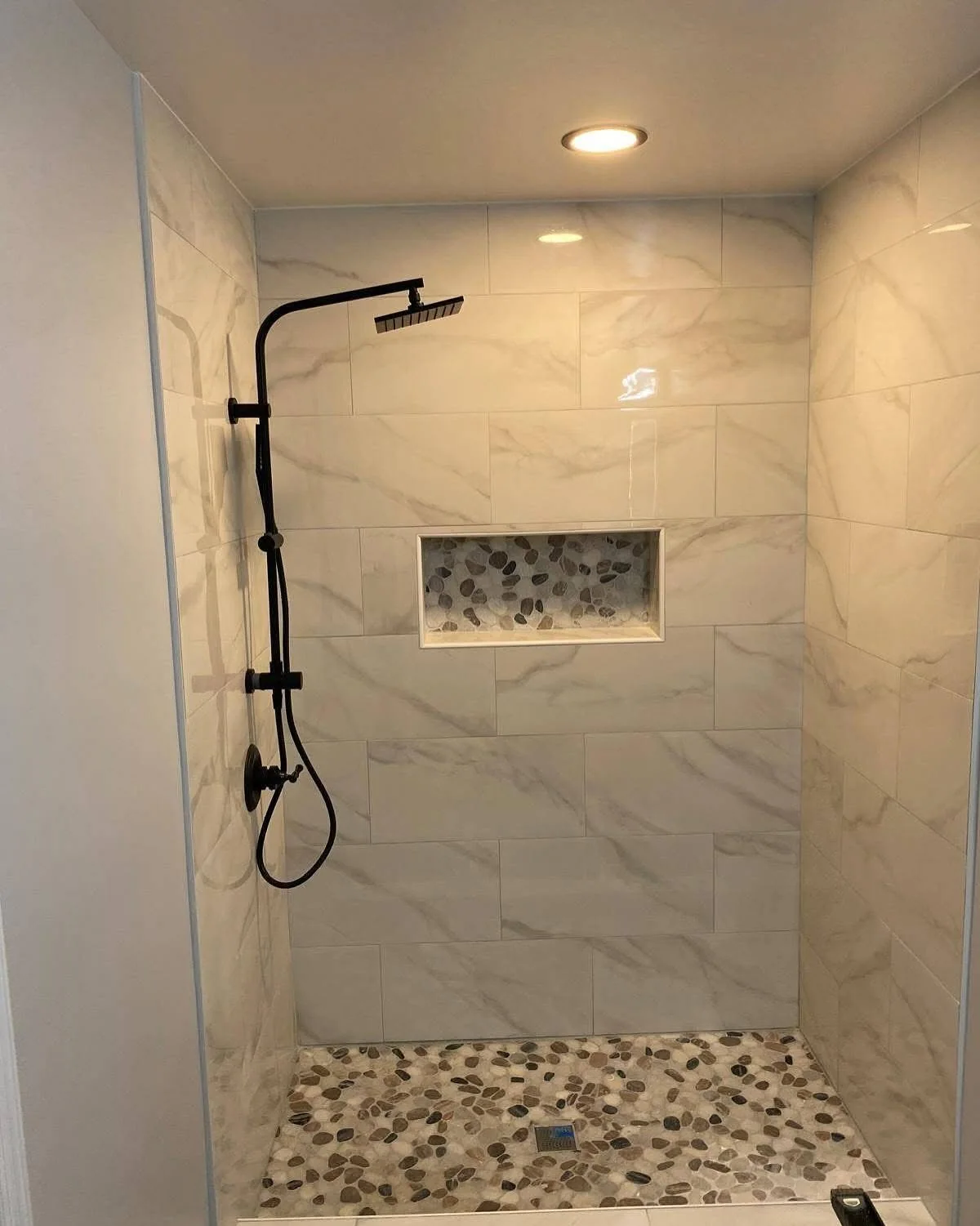 Marble-look tiled shower with mosaic floor, recessed niche, and dark fixtures